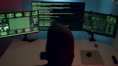 Karanlık bir odada siber bir suçlu yüksek güvenlikli ağları hacklemek için birden fazla ekranda çalışır. Veri ihlali ve çevrimiçi güvenlik tehdidi kavramı.
