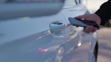 Telefonu araba sapına yaklaştıran bir kişinin yakın çekimi ve uygulama kapıyı açıyor. Modern akıllı araba kavramı. Beyaz araba mobil bir uygulama kullanılarak kolayca açılabilir..