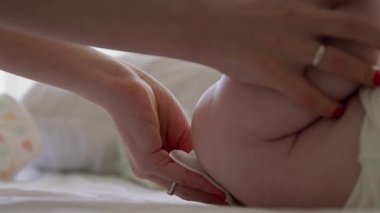 Kimliği belirlenemeyen bir annenin narin elleri, yeni doğanların popolarını hassas ve çevre dostu bir mendille siliyor. Annenin bebek bezini değiştirirken ve organik ürünler kullanırken yakın plan görüntüsü.