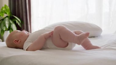 Tombul bebek masajdan sonra rahat ve hareketli yatakta uzanmış, kollarını ve bacaklarını sallıyor. Bilinmeyen beyaz elbiseli bebek, evinin sessiz vahasında yatağında sırt üstü yatıyor.
