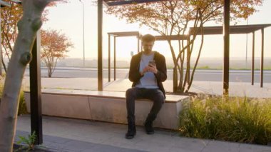 Genç serbest çalışan bir adam gün batımı ışığında bankta oturuyor telefonuna bir mesaj yazıyor ve uzaktan çalışıyor. Adam telefonunu internet ağlarındaki işi için kullanıyor. Çocuk mesajlara cevap verir