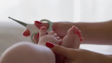 Yeni doğmuş bir bebeğin sabah ışığında çıplak ayakla çekilmiş yakın plan görüntüsü. Annenin elleri bebek rutin bakımını yapıyor ve özel bebek makasıyla bebek tırnaklarını kesiyor..