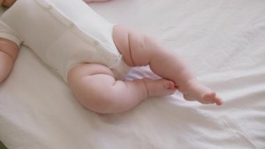 Tombul bebek masajdan sonra rahat ve rahat bir şekilde rahatladı. Üst manzara, yakın plan, beyaz kolsuz tulumlu bebek, sırt üstü yatıp bacaklarını tekmeliyor..