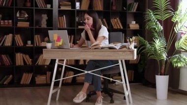 Okul tezini dizüstü bilgisayarla hazırlayan güzel bir öğrenci. Zeki genç bir kadın, bir masanın arkasında oturmuş modern tasarımı olan boş bir halk kütüphanesinde online kurs okuyor.