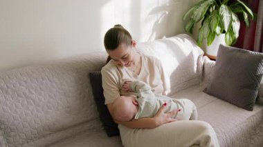 Mutlu kadın bebeğini göğsüne dayayıp onu anne sütüyle besliyor, gülümsüyor, bebeğe huzur ve güvenlik teklif ediyor. Genç ve güzel anne, bebeğini evde emzirme sürecinin tadını çıkarıyor.