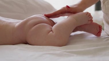Karnının üzerinde çıplak tombul bir bebeğin yakın plan görüntüsü. Bir anne nazikçe bebeğin poposuna krem sürerek nazikçe masaj yapar. Çıplak ve tombul bebek uzanmış, rahatlamış.