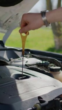 Çubuklu adam motor yağı seviyesini kontrol ediyor. Özel bir alet tutan adam, sıvıyı analiz etmek için uzun metal çubuğu halkayla dibe indiriyor.