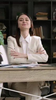 Ofisteki işyerinde hizmet vermeye hazır neşeli bir kadın yönetici. Yüzünde dostane bir ifadeyle gülümseyen genç kadın ve çapraz kollar işi seviyor.