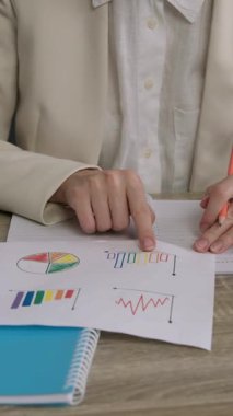 Ofis çalışanı, günışığıyla aydınlatılan grafik ve diyagramlarla belgeleri analiz eder. Çalışan grafiklerde gösterilen verilerdeki tutarsızlıkların altını çizmek için kalem kullanır