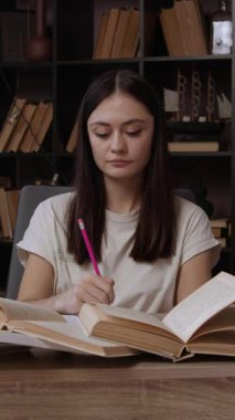 Meraklı kız ödevini kitaplardan öğrenerek ve internetteki bilgisayarı kullanarak hazırlıyor. Genç esmer kadın, bir ofis masasında güzel bir ofiste ders çalışıyor..