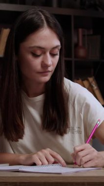 İlgilenen kız internette yararlı bilgiler arıyor ve kalemle not defterine not alıyor. Genç esmer, bir ofis masasında bilgisayar ve internet kullanarak ders çalışıyor..