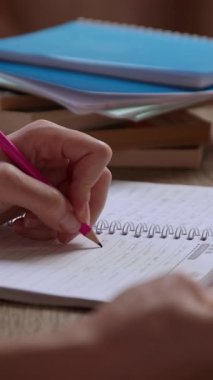 Not defterindeki kalemle not alan ve yazan genç bir kadının yakın plan görüntüsü. Öğrenci kavramı, öğrenciler, çalışmalar, sınavlar, sınavlar, öğrenme. Kitaplı ofis masası