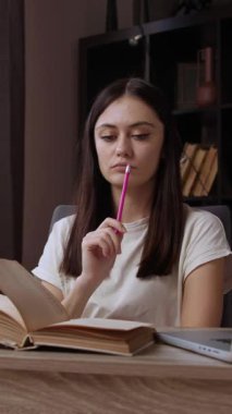 Konsantre ve düşünceli bayan öğrenci masada birkaç açık kitap okuyarak ev ödevini hazırlıyor. Esmer öğrenci modern bir ofiste okulda öğrenim görüyor.