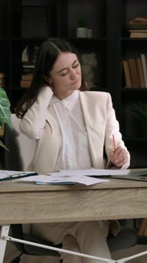 Genç bayan muhasebeci yoğun bir şekilde bilgisayarda ve belgelerde çalışıyor. Ofis masasında oturan genç esmer kadının sırtı ağrıyor. Günlük oturma işinden dolayı boynu ağrıyor. Belgelerle birlikte ofiste çalış.