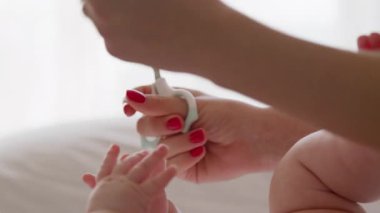 Sabahın ilk ışıklarındaki çıplak bir bebeğin yakın plan görüntüsü. Annenin elleri bebeğin rutin bakımını yapıyor ve özel bebek makasıyla tırnaklarını kesiyor.