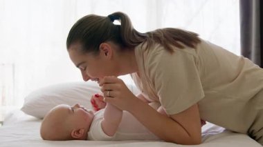 Yan görüş, genç ve mutlu anne sabah rutinini yapıyor bebeğine bakıyor ve onu neşelendiriyor. Gülümseyen kadın nazikçe burnunu onun sırtında yatan mutlu bebeğin burnuna değdirir.
