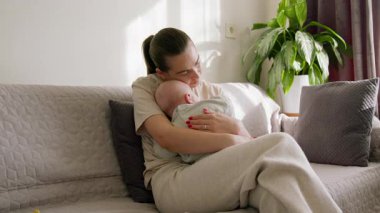 Genç, mutlu anne kucağında bir huzur ve sevgi vahasında bebeği tutuyor. Sevgi dolu anne, çocuğunu nazikçe okşayarak kollarında uyutur. Sabah güneşi. Mutlu annelik