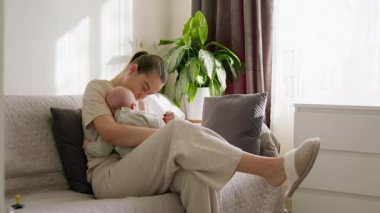 Güzel genç anne, huzurlu bebeğiyle sabahın sessizliğinin tadını çıkarıyor. Mutlu anne bebeğini göğsüne yakın tutup sevgi, güven ve huzur sunuyor. Anne-çocuk bağı