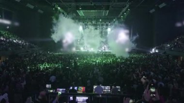 Telefonlar karanlık konser salonunda parlıyor, geniş görüşlü. İnsanlar eğlence etkinliklerinde telefonda video çekerek kalabalıklaşıyor. Sahne ışıkları altında seyirci siluetleri parlıyor. Disko gece kulübünde titreşimli ışık gösterisi