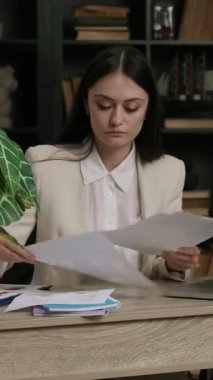 Yorgun şirket müdürü birkaç önemli belgeyi inceliyor. Minimalist ofiste yeşil çiçekli bir kadın modern ve çağdaş bir ofis masasında oturuyor.