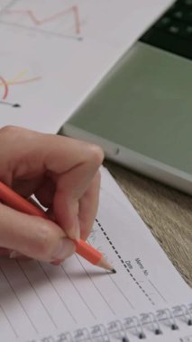 Solak bir kadın ofiste dizüstü bilgisayarla günlüğe notlar yazıyor. Kadın girişimci, partneriyle çevrimiçi müzakerelere hazırlanıyor