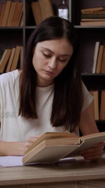 Güzel esmer kız eski bir kitap okuyor ve defterinde bir kalemle not alıyor. Sessiz ve güzel bir odada bir ofis masasında oturan genç kadın bir kitap okuyor.