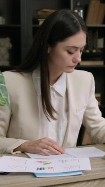 Klasik takım elbiseli öğrenci stajyer bir ofis masasında oturuyor. Kadın birkaç şirketin istatistik ve grafiklerini analiz ediyor ve birkaç büyüme stratejisi oluşturmayı düşünüyor. İş geliştirme şirketi.