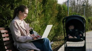 Bebek arabasında sessizce otururken parkın dışındaki bilgisayarda sandalyeye oturmuş yazı yazan şık genç bir kadın. Boş zamanlarında internetten doğum izninde olan bir kadın.