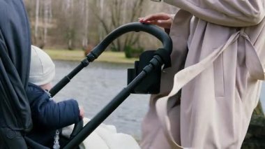 Bebek arabası için bir bardak tutucunun yakın plan görüntüsü. Anne bebeğiyle parkta yürüyor, kahvenin tadını çıkarıyor ve bebek arabasındaki bardak tutacağına koyuyor. Annem işe yarar şeylerle doğum yapmayı sever.