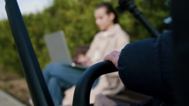 Annesi bilgisayarla uğraşırken, bebek arabasının içinde sessizce oturan bebek ellerinin yakın plan bulanık görüntüsü. Kadın boş zamanlarında internette uzaktan çalışıyor. Annelik ve iş arasındaki denge