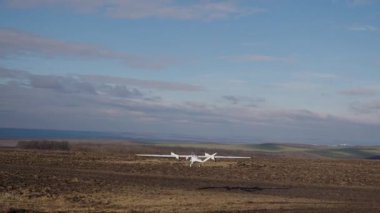 Beyaz İHA açık alanların üzerinden yüksek irtifada havalanıyor. Drone uzun mesafelerde tarım arazilerini filme alır. Şehrin dışındaki tarım arazileri, açık hava, açık gökyüzü. Teknoloji ve tarım alanlarındaki yenilikler.