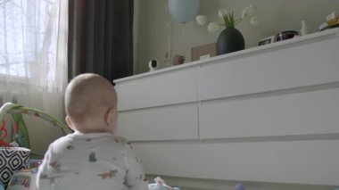 Halıda oturan bir bebeğin arka planda oturması, güzel dekore edilmiş odasında oyuncaklarla oynaması. Meraklı bebek sabahları tek başına sessizce oynuyor.