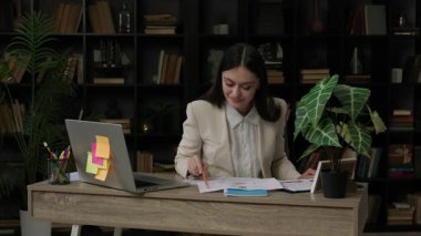 Gülümseyen ve birkaç finansal belgeyi analiz eden mutlu kadın avukat. Finansal hukukta uzmanlaşmış genç bir profesyonel rezonans dosyası üzerinde çalışan bir ofis masasında çalışıyor.