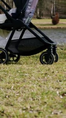 Bir annenin bebeğini şık, modern ve rahat bir bebek arabasıyla gezdirdiği yakın plan görüntüsü. Kadın, çimde bebek arabasıyla yürüyor ve doğum izninde doğanın tadını çıkarıyor.