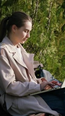 Bebek arabasında sessizce otururken parkın dışındaki bilgisayarda sandalyeye oturmuş yazı yazan şık genç bir kadın. Boş zamanlarında internetten doğum izninde olan bir kadın.