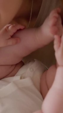 Gülümseyen ve bebek gibi elleriyle ve ayaklarıyla sırtüstü uzanan mutlu genç annenin yakın plan görüntüsü. Aktif ve neşeli tombul bebek. Anne, bebeğine evde sevgi ve güven sağlıyor.