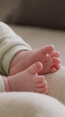 Annesinin kollarında yatan çıplak ayaklı bir bebeğin yakın çekimi. Aktif çocuk küçük elleri ve ayaklarıyla tek başına oynuyor. Sabah güneşinden gelen D vitamininin tadını çıkarıyorum. Sağlıklı çocuk hayattan zevk alıyor