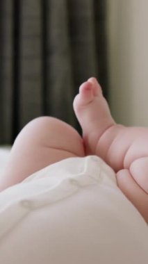 Beyaz bir tulumla yatakta uzanan tombul bir bebeğin yakın çekimi, mutlu ve aktif, bacaklarını ve kollarını tekmeliyor. Bebek doğrudan sabah güneşinden D vitamini alır. Sağlıklı bebek hayatın tadını çıkarır.