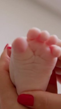 Yeni doğmuş bir bebeğin çıplak ayakla yakın çekimi. Anneleri yabancı eller, bebek ayağının tabanına hassas hareketlerle masaj yapıyor. Banyodan sonra genç anne bebeğe nemlendirir ve masaj yapar.