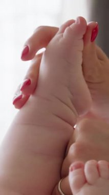 Yeni doğmuş bir bebeğin çıplak ayakla yakın çekimi. Anneleri yabancı eller bebek ayaklarının tabanına nazikçe masaj yapıyor. Genç anne bebek ayaklarının tabanını öpüyor. Evde yeni doğan bakımı rutini