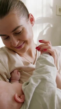 Mutlu anne bebeğe bakarak gülümsüyor. Genç anne küçük çocuğunu kollarında tutuyor ve evde çocuğuyla oynayıp anneliğin tadını çıkarıyor. Anne, bebeğin elini öpüyor.