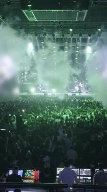 Telefonlar karanlık konser salonunda parlıyor, geniş görüşlü. İnsanlar eğlence etkinliklerinde telefonda video çekerek kalabalıklaşıyor. Sahne ışıkları altında seyirci siluetleri parlıyor. Disko gece kulübünde titreşimli ışık gösterisi