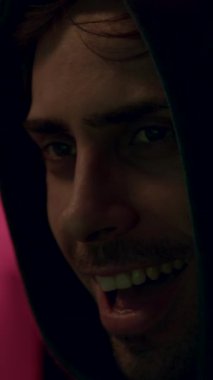 Kapüşonlu bir hacker 'ın tehlikeli yüzü gülerken, dizüstü bilgisayarda klavye yazarken ve şifreleri kırarken. Tehlikeli kapüşonlu bilgisayar korsanı sisteme siber virüs bulaştırıyor..