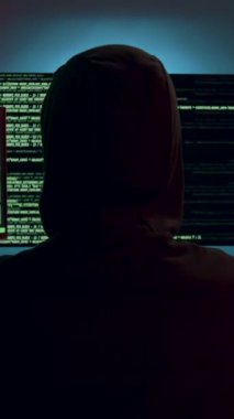 Kapüşonlu genç bir bilgisayar korsanı loş bir odada üç monitörden hızlıca izliyor. Ekranlar güvenlik ihlali ve hackleme girişimleri gösteriyor. Siber Suçlar ve Siber Güvenlik kavramı.