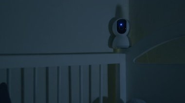 Bebek beşikten sarkan güvenlik kamerası o uyurken bebeği izliyor. Geceleri kablosuz ağ ile modern dijital cihaz bebek odasını ve beşiğini izliyor. Güvenlik ve güvenlik.