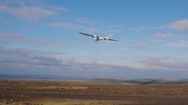 Uçak şeklinde beyaz bir dron havada uçuyor ve yere iniyor. Drone videoyu gerçek zamanlı kaydediyor ve kontrol merkezine gönderiyor. Nüfus güvenliğinin uzaktan izlenmesi