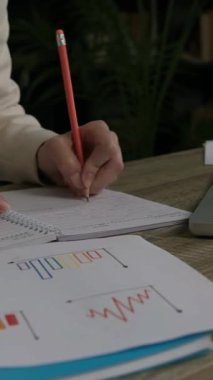 Nitelikli kadın ofis çalışanı dizüstü bilgisayardaki verileri analiz eder. Solak iş kadını defterine kurşun kalemle detaylı notlar yazar.