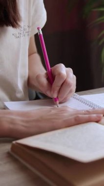 Not alan ve bir defterden çizim yapan bir kızın yakın plan resmi. Kitaplar ve defterlerle dolu bir ofis masası. Öğrenci ev ödevini hazırlıyor ve huzur ve rahatlık vahasında çalışıyor.