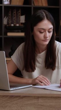 Genç esmer kız internette bilgi arıyor ve kalemle deftere yazıyor. Modern bir ofiste ofis masasında neşeli bir öğrenci ders çalışıyor. Öğrenim kavramı