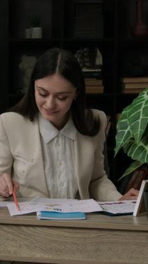 Gülümseyen ve birkaç finansal belgeyi analiz eden mutlu kadın avukat. Finansal hukukta uzmanlaşmış genç bir profesyonel rezonans dosyası üzerinde çalışan bir ofis masasında çalışıyor.